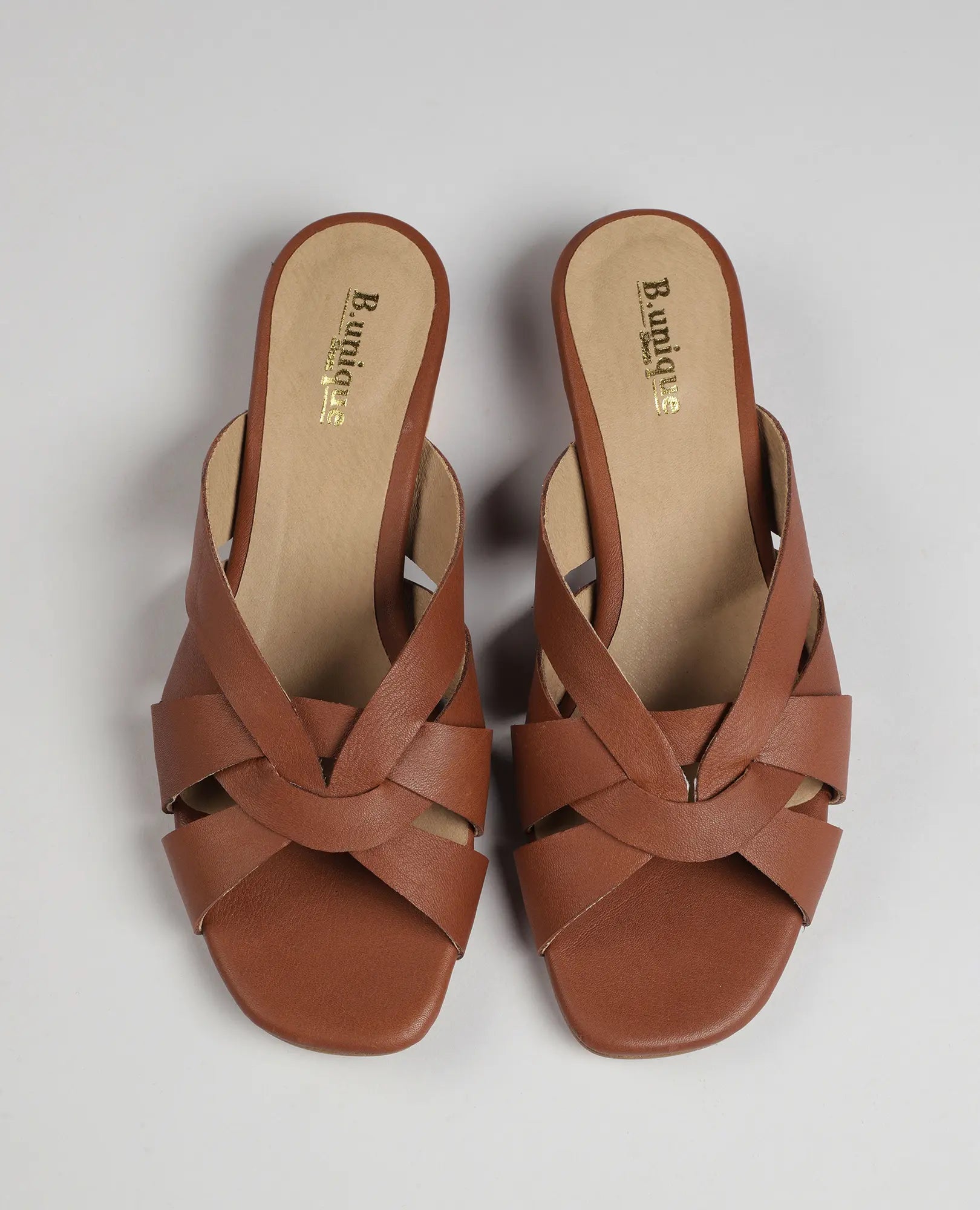 B.unique כפכפים עם רצועות משולבות - סאלי: כפכפים עם עקב נמוך מעור חום קלוע, צילום על רקע בהיר.