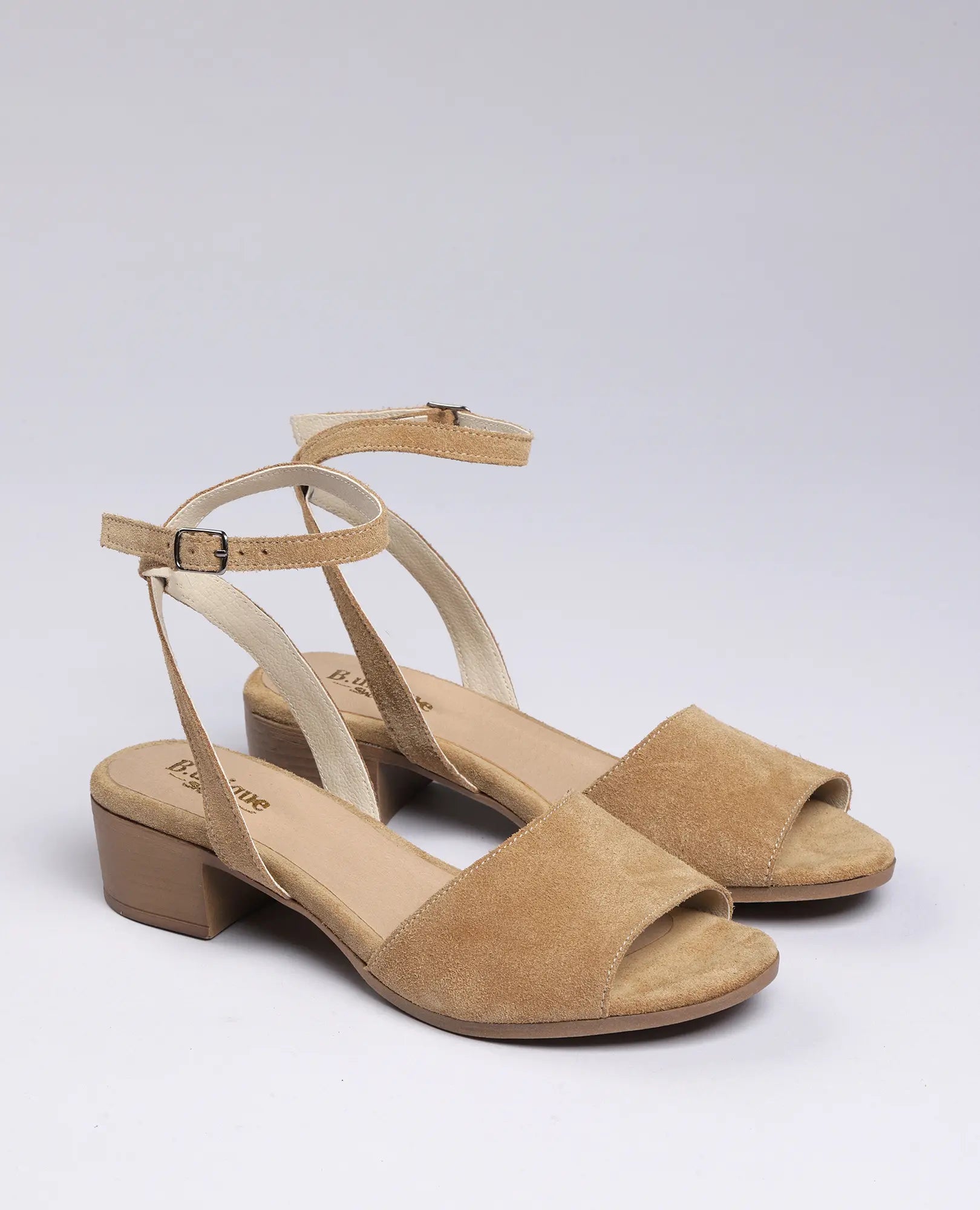 סנדלי פלה זמש-סנואו של B.unique לנשים, עם רצועות קרסול ועקב נמוך, מוצגים על רקע בהיר.