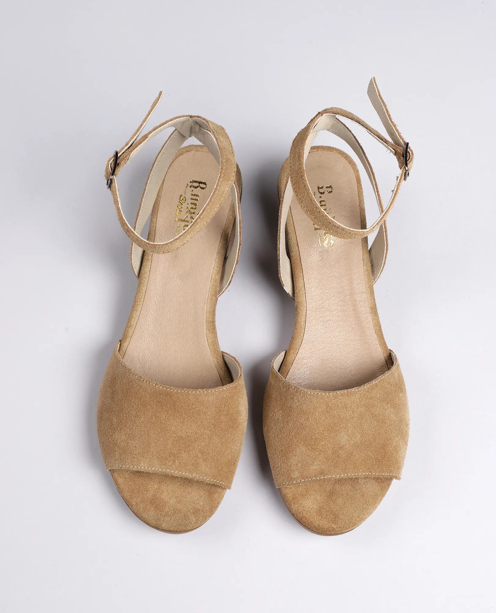 סנדלי פלה זמש-סנואו של B.unique בצבע קאמל עם רצועות קרסול, מוצגים על רקע בהיר ופשוט.