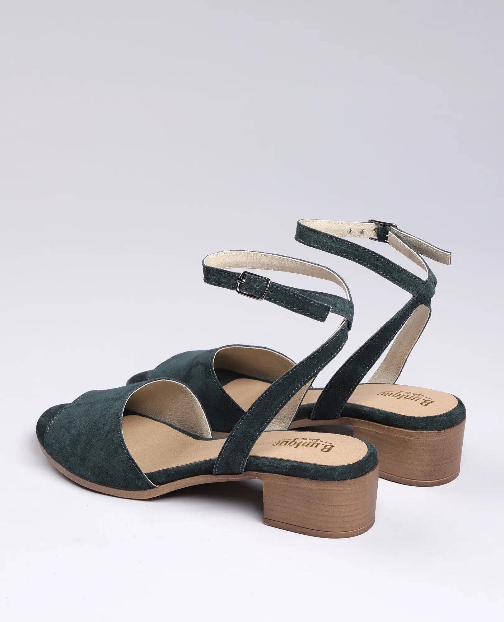 B.unique סנדלי פלה זמש-סנואו: סנדלים ירוקים לנשים עם רצועות קרסול ועקב עץ, מוצגים על רקע חלק.