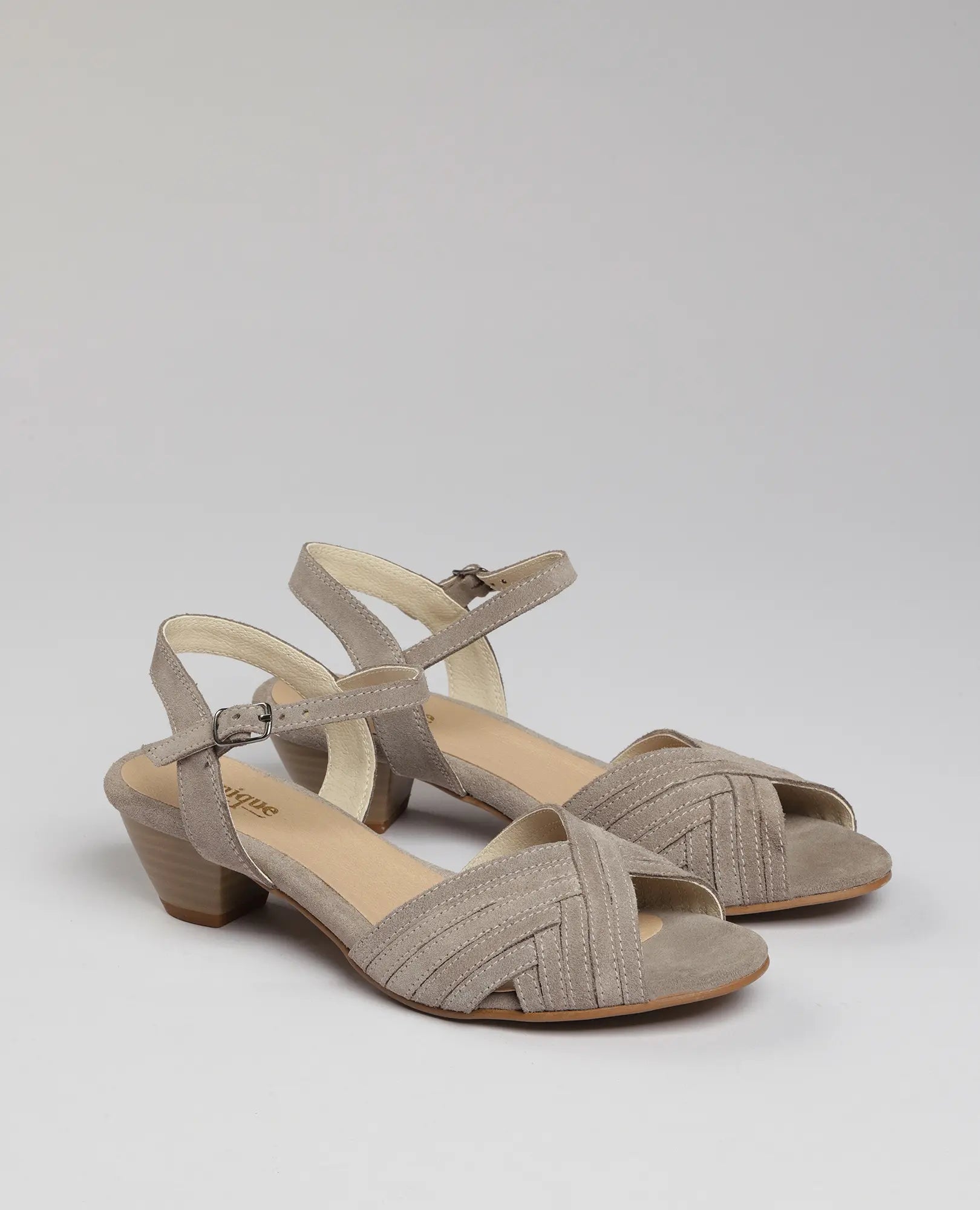 סנדלי עקב "אלואיז" מבית B.unique, מעור איכותי בצבע טאופ, עם רצועות קרסול ועקב בלוק נמוך.