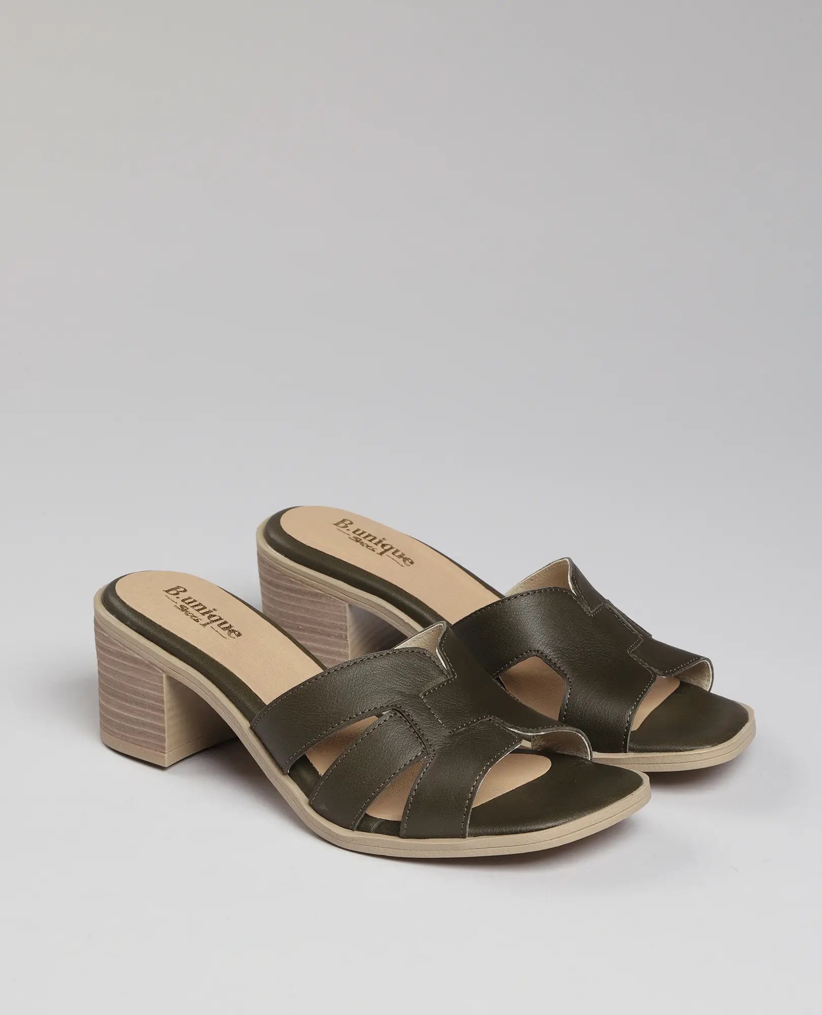 זוג כפכפי עקב-ניבר של B.unique בצבע ירוק זית, עם אצבעות פתוחות ועקבים מעץ, מוצגים על רקע אחיד.