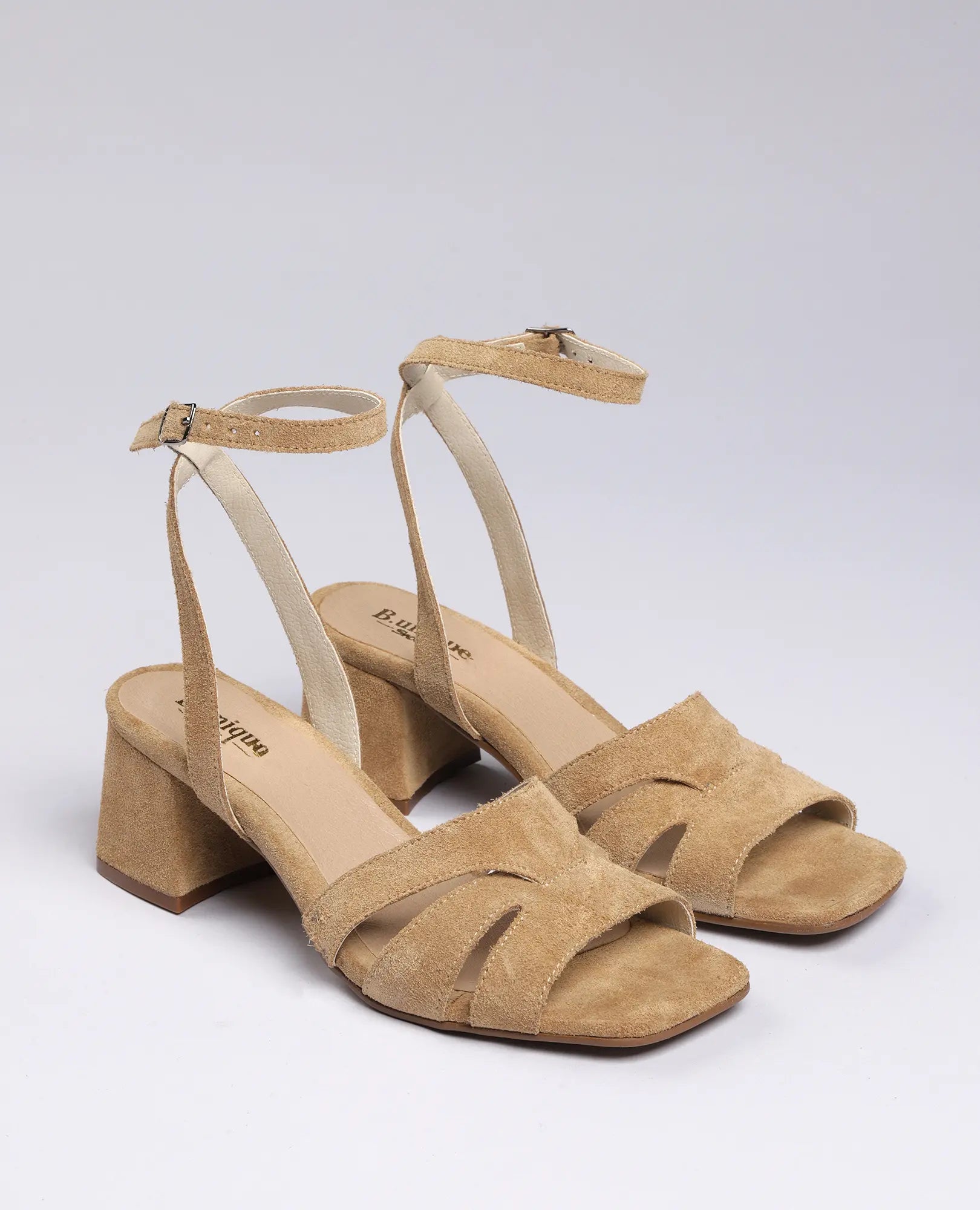 זוג סנדלי עקב "ארבל" בצבע בז' מעור זמש מבית B.unique עם רצועת קרסול, על רקע לבן חלק.