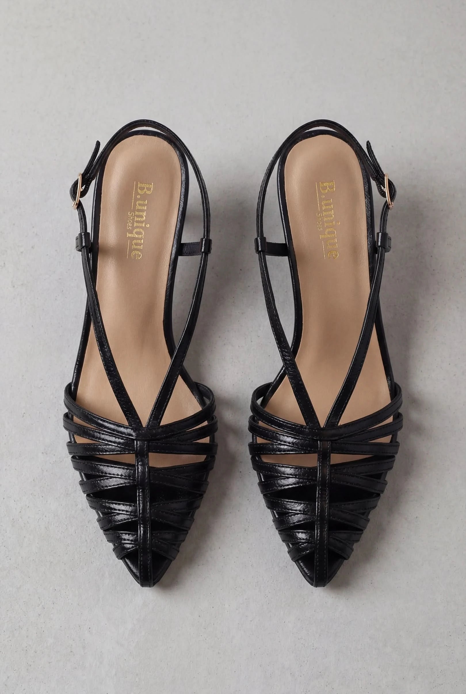 סנדלי עקב- מיכאלה: זוג סנדלי עקב אלגנטיים בצבע שחור, מעור, עם רצועות דקות ועקב מחודד, גפה פתוחה ורפידות בגוון בז’ עם חותמת Boutique בזהב—מוצגות על משטח אפור בהיר.