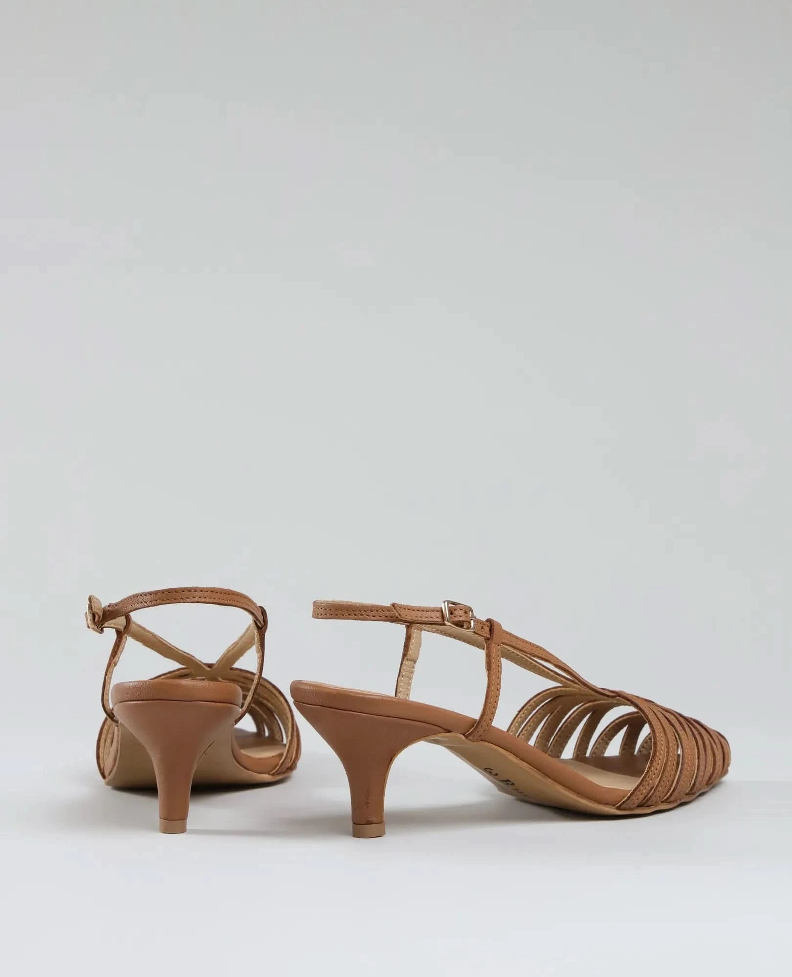 סנדלי עקב- מיכאלה: זוג סנדלים בגוון טאן עם עקב קיטן נמוך, רצועות בעקב ובקרסול, ועיצוב פתוח לאירועים אלגנטיים. מוצגים על רקע אפור בהיר.