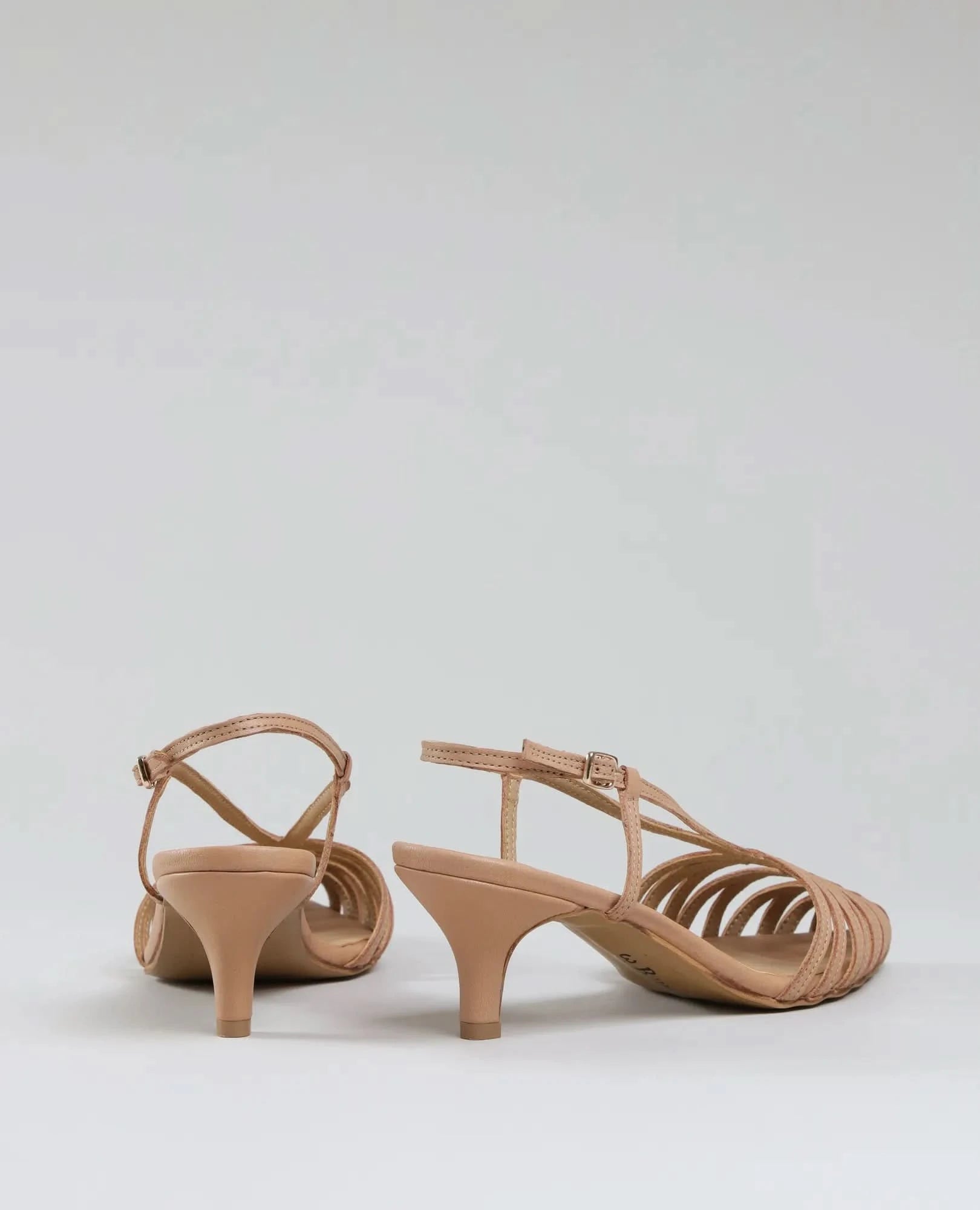 A pair of beige סנדלי עקב- מיכאלה strappy heeled sandals with kitten heels, displayed from the back and side on a plain light background. One sandal stands upright; the other is slightly tilted.