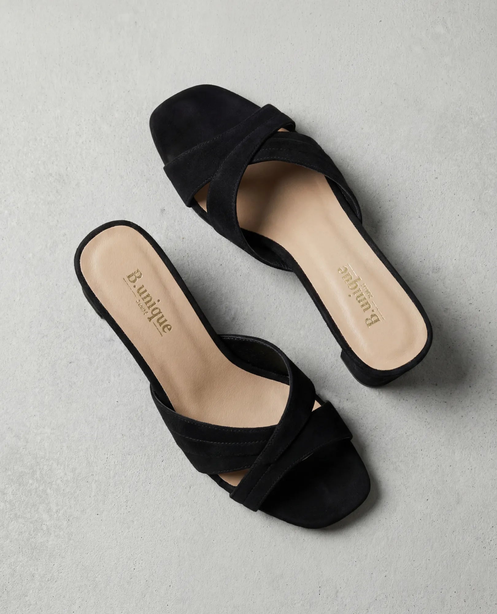 זוג כפכפי עקב בצבע ארגמן מבית B.unique, עם רצועות מצטלבות ורפידות בצבע בז' על גבי משטח אפור בהיר.