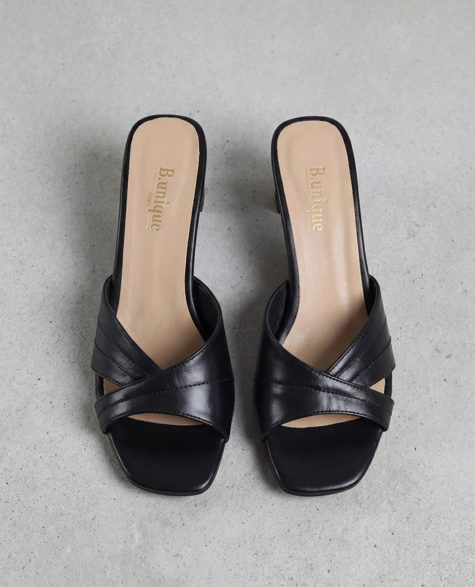 זוג כפכפי עקב של B.unique בצבע ארגמן, מעור איכותי בצבע שחור, עם רצועות מצטלבות, מוצגים על רקע אפור בהיר.