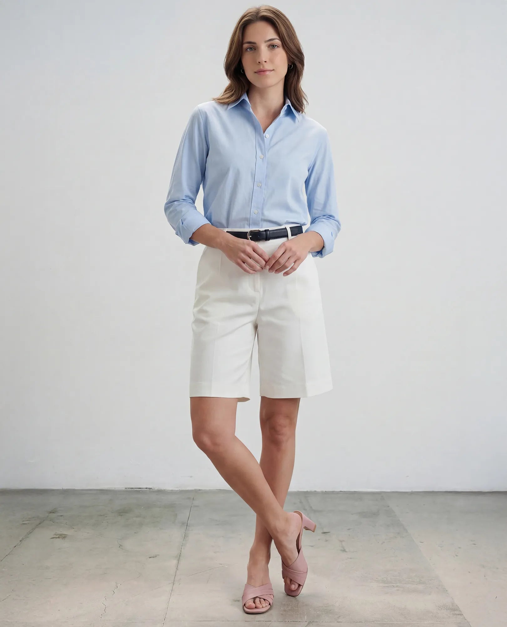 אישה לבושה בחולצה תכלת, מכנסיים קצרים לבנים באורך הברך וכפכפי עקב בצבע ארגמן של המותג B.unique, עומדת על רקע אחיד.