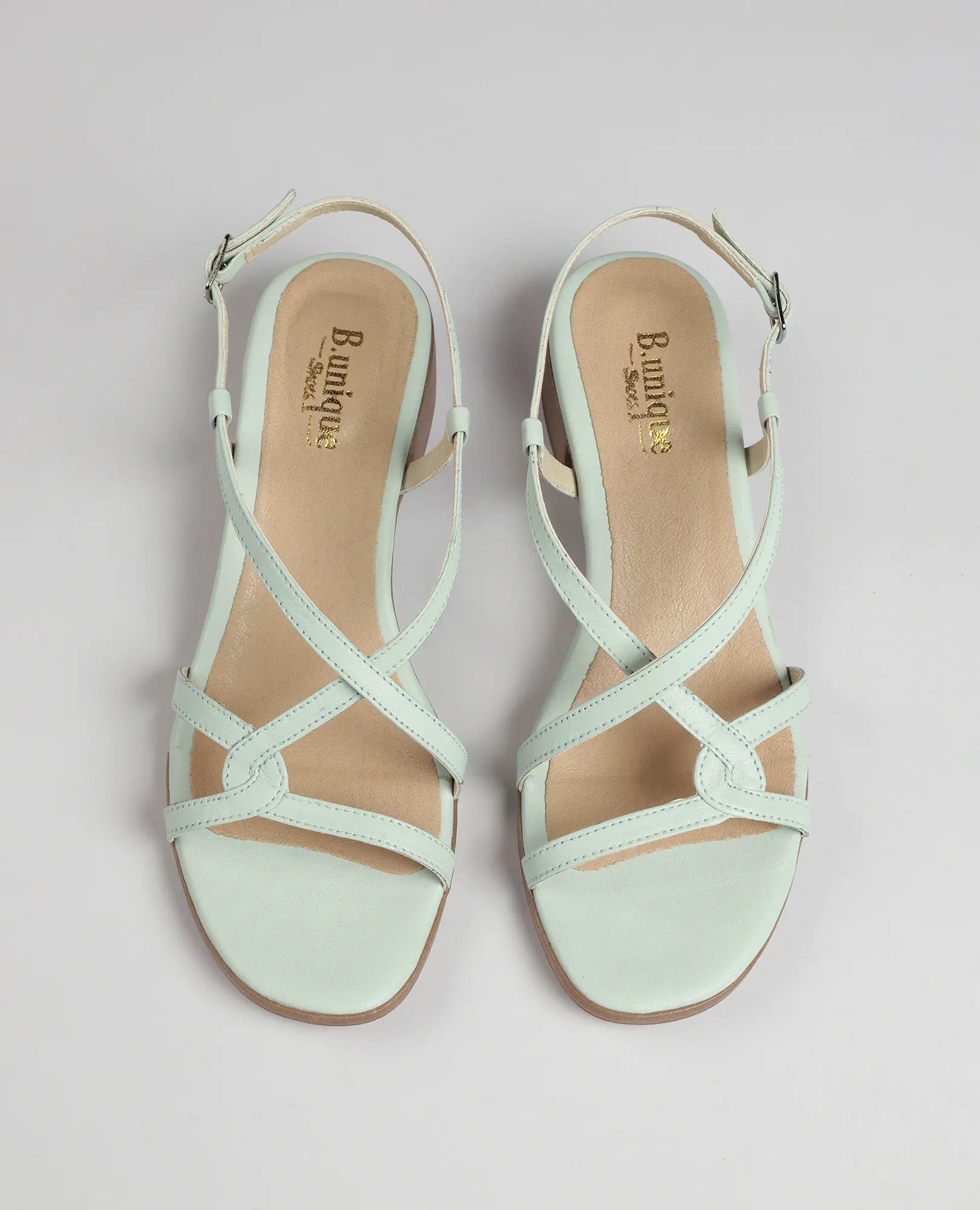 זוג סנדלי רצועות איקס-מולי של B.unique בצבע מנטה, עם עקב נמוך ורצועות קרסול, על רקע בהיר.