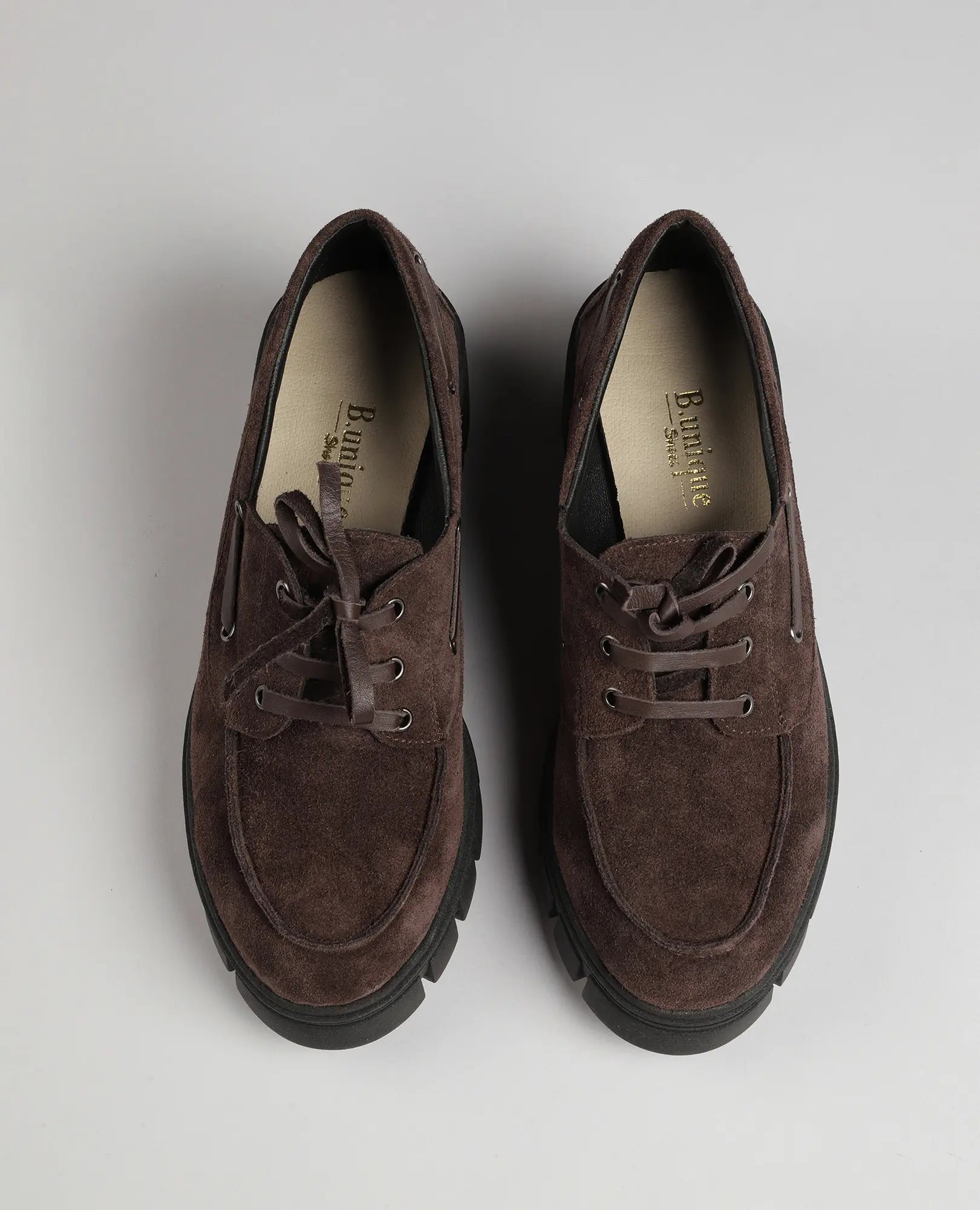 זוג נעלי אוקספורד-לאסי חומות מבית B.unique עם סוליות שחורות עבות, במבט מלמעלה על רקע אפור בהיר.