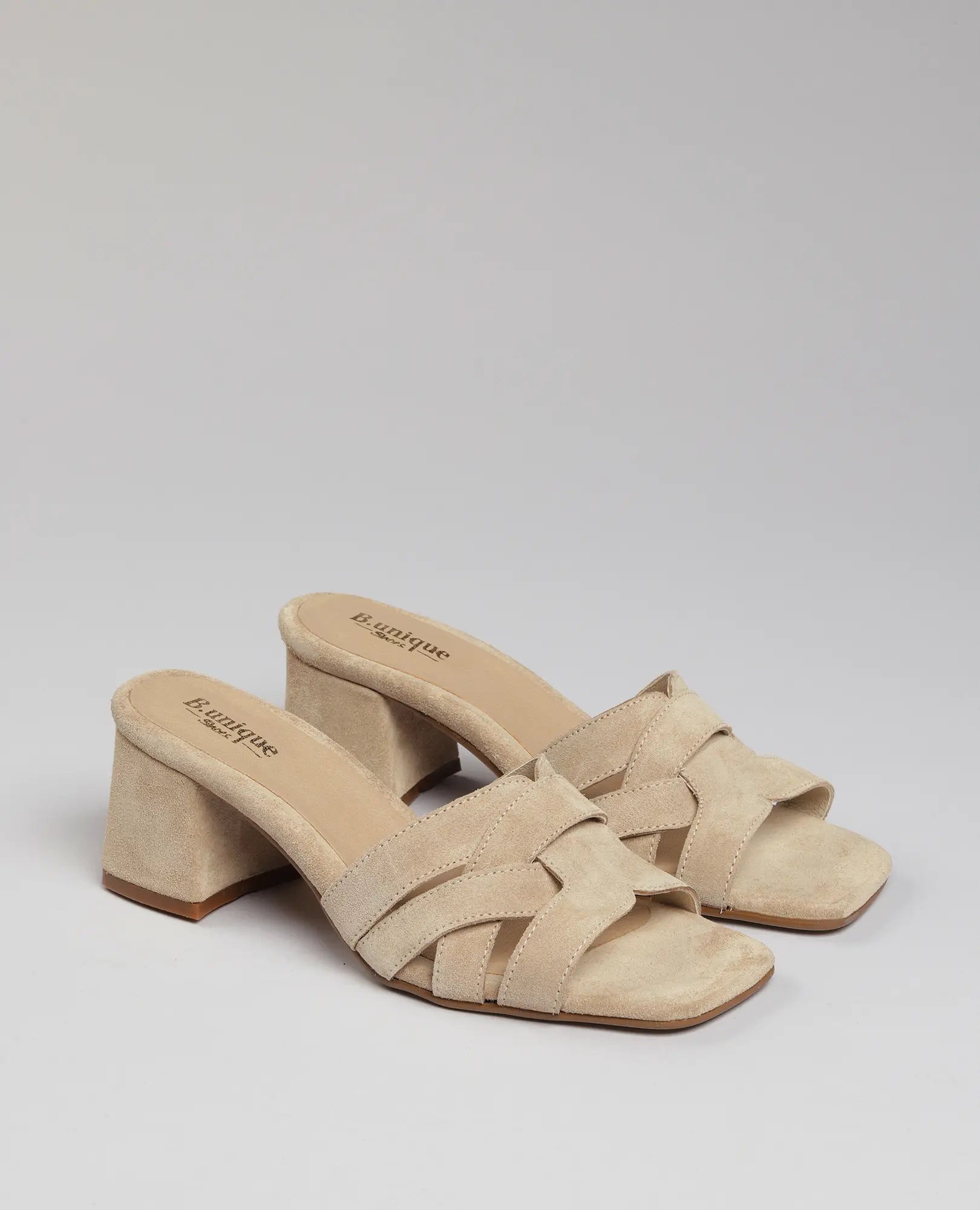 כפכפי עקב מרגי מבית B.unique בצבע טאופ, עם עקב רחב, רצועות קלועות ועיצוב פתוח באצבעות.