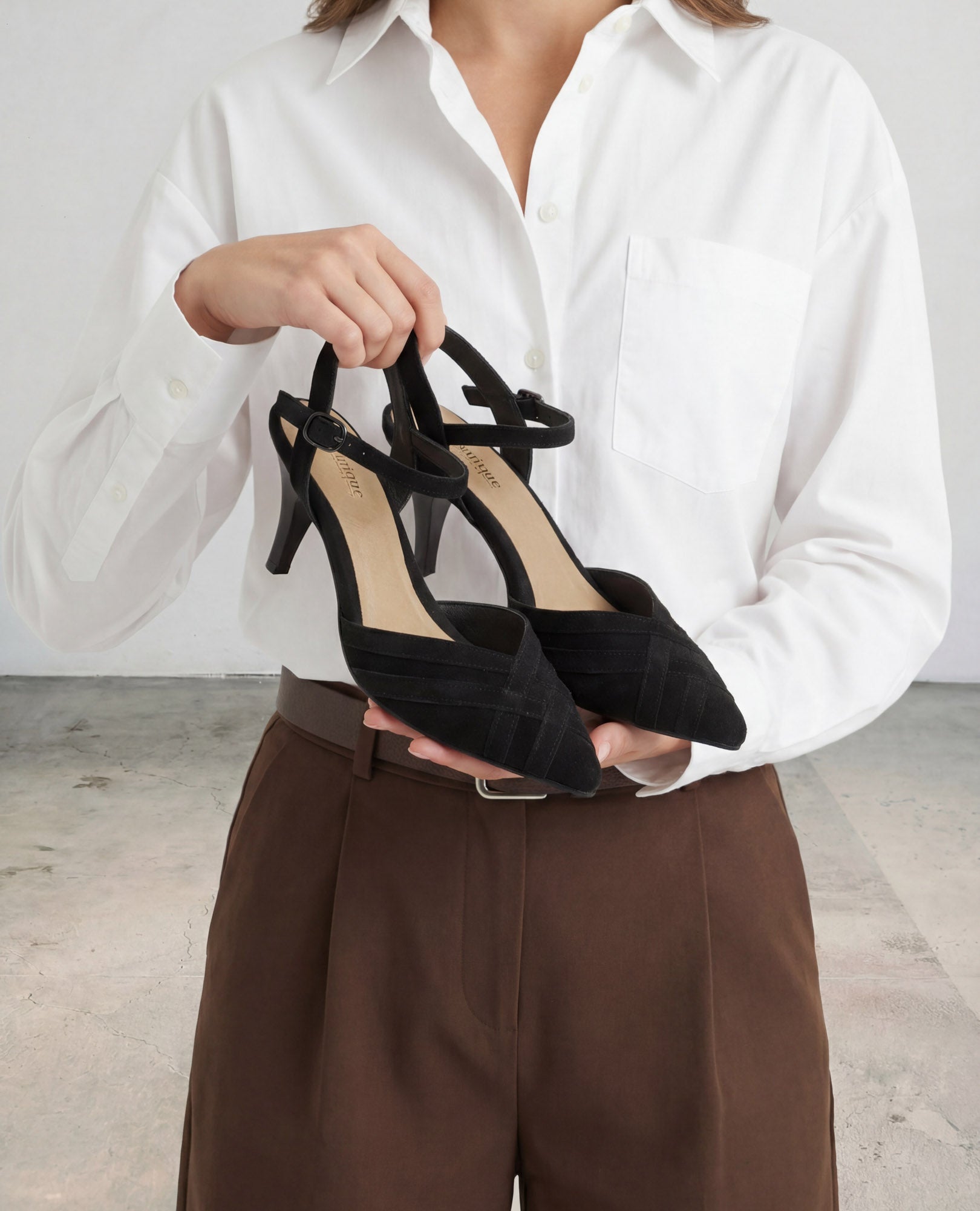 אדם לבוש בחולצה לבנה ומכנסיים חומים נועל נעלי עקב שחורות מדגם "איימי" של B.unique.