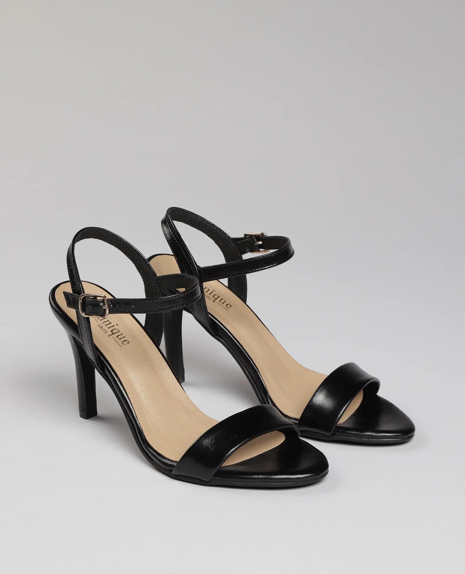 סנדל עקב גבוה-גלן לנשים מבית B.unique, עם רצועות קרסול בעיצוב אלגנטי על רקע אפור בהיר.