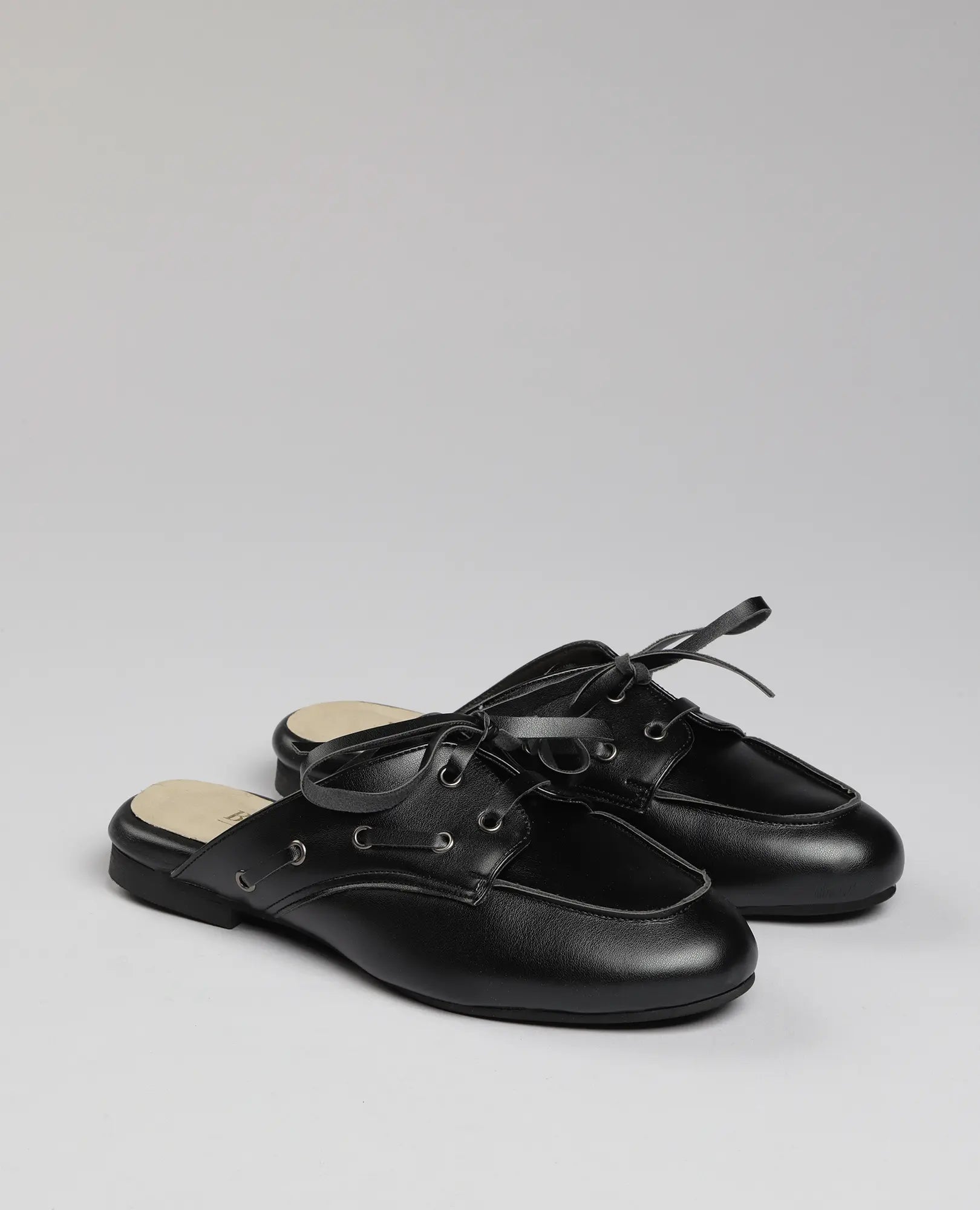 כפכפי מוקסין- לירי שחורים של B-Unique VEGAN עם שרוכים דקורטיביים על רקע אפור בהיר אחיד.