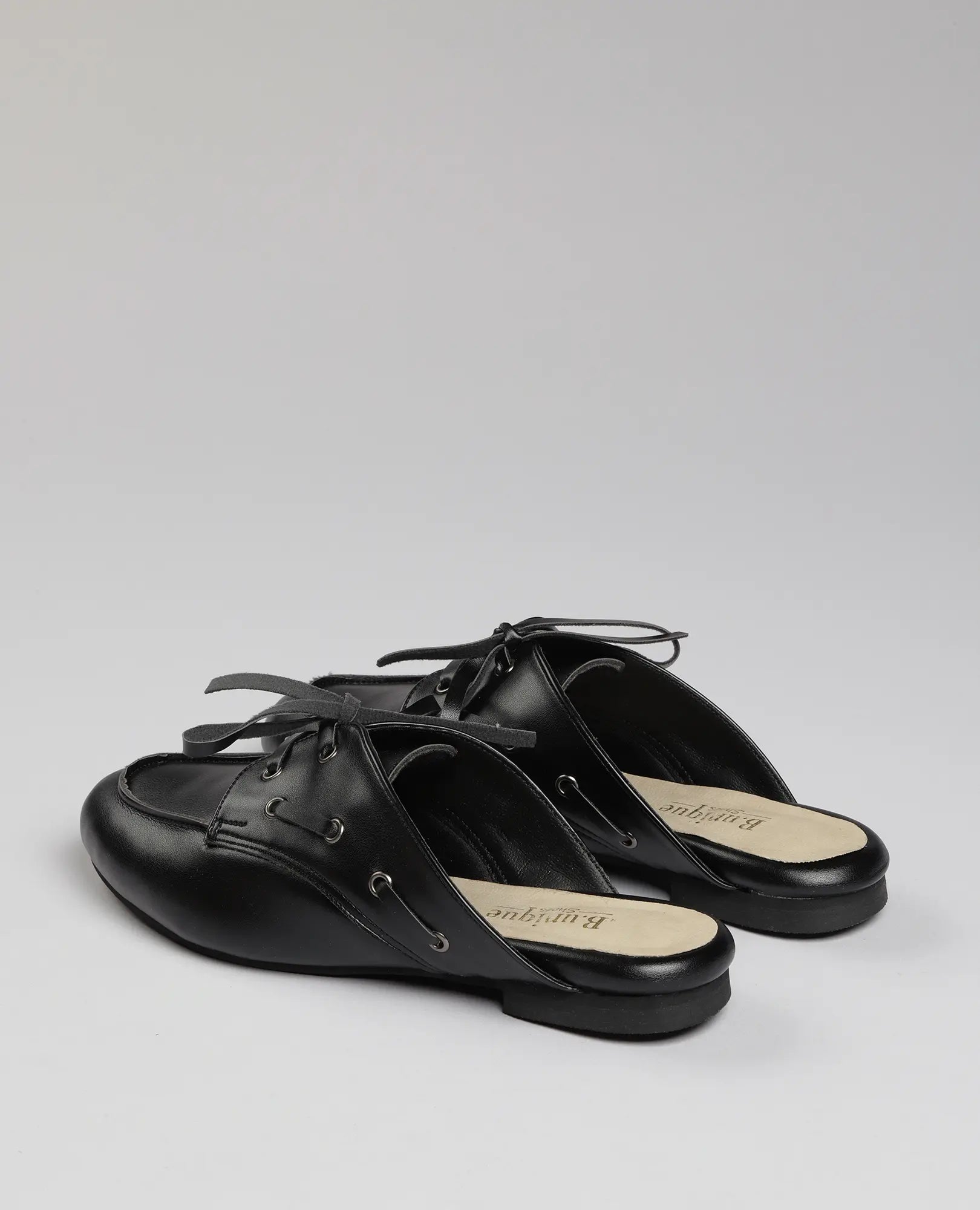 כפכפי מוקסין- לירי דמוי עור שחורות עם שרוכים ורפידות בז' של B-Unique VEGAN על רקע אפור בהיר.