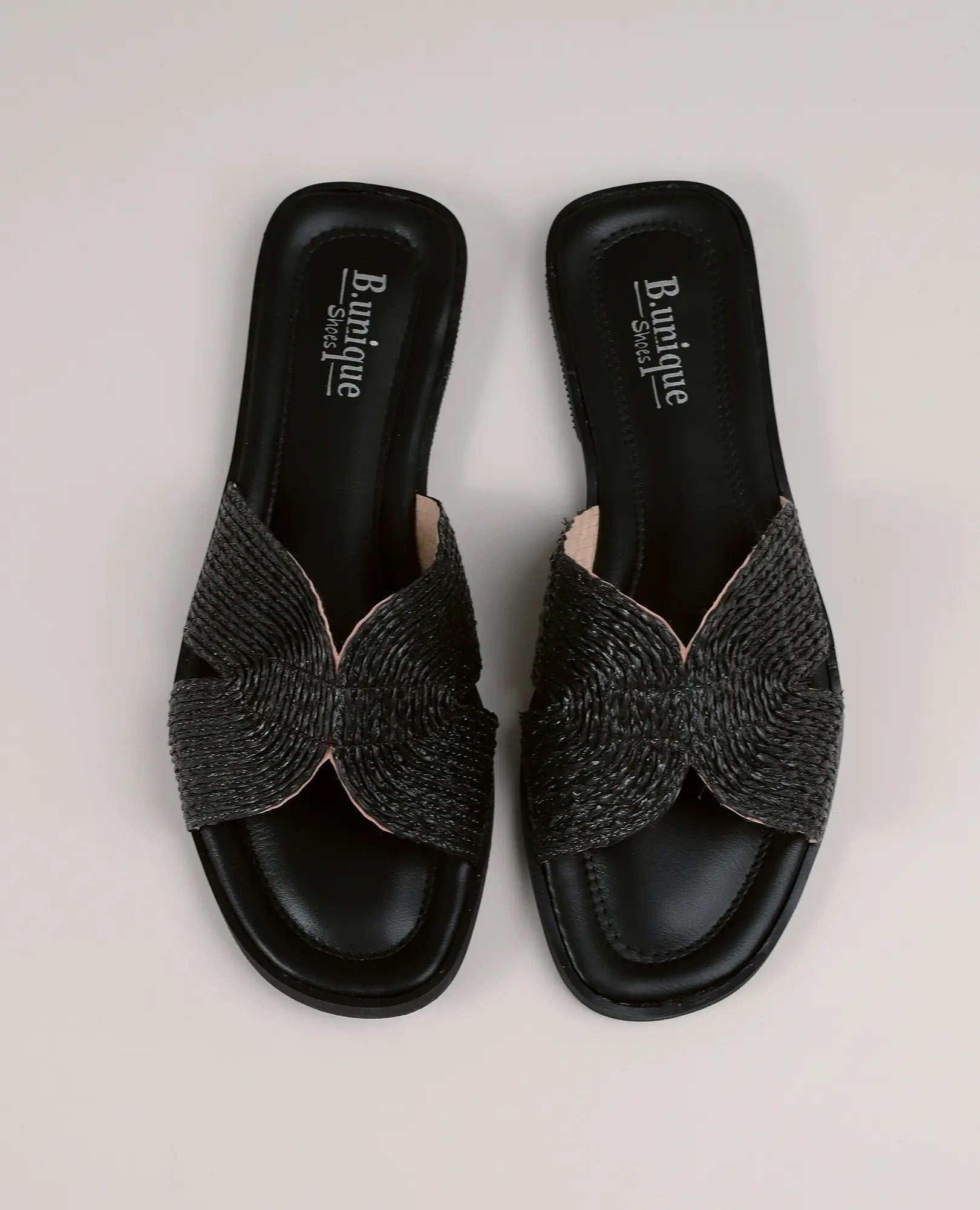 כפכפי רפיה - דגם אלינוי של B-Unique VEGAN בצבע שחור עם רצועות קלועות שטוחות בעיצוב צלב על רקע בהיר.