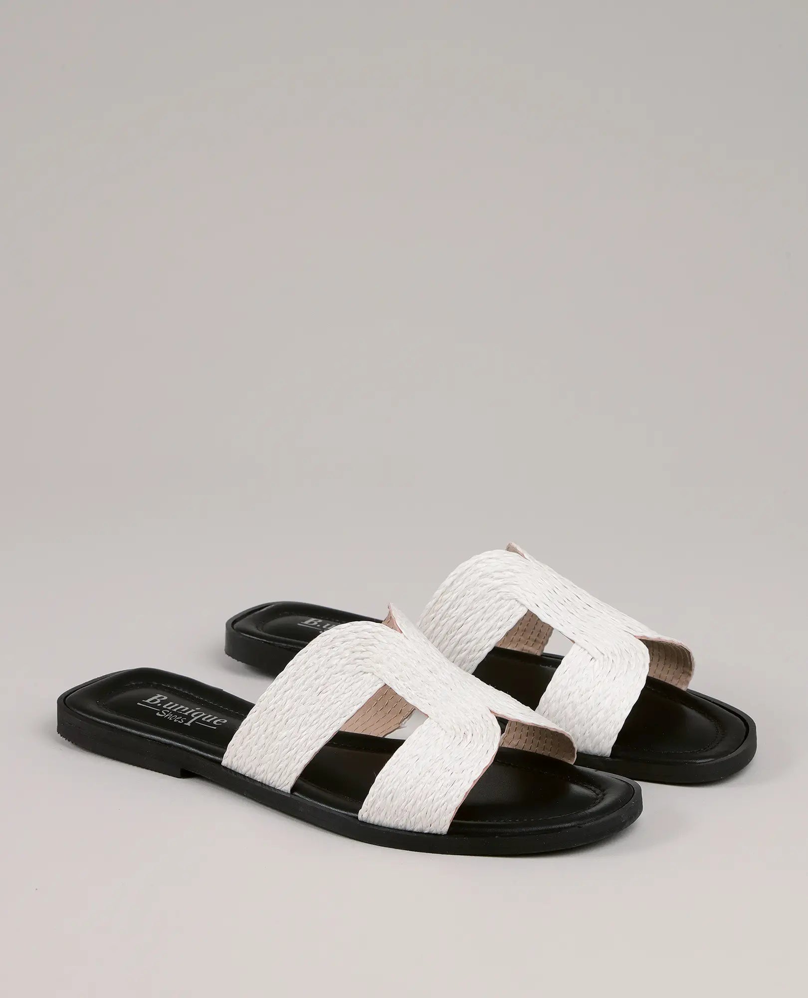 זוג כפכפים מדגם B-Unique VEGAN רפייה דקה-אליאור, עם רצועות לבנות רחבות ושזורות על רקע בהיר וחלק.