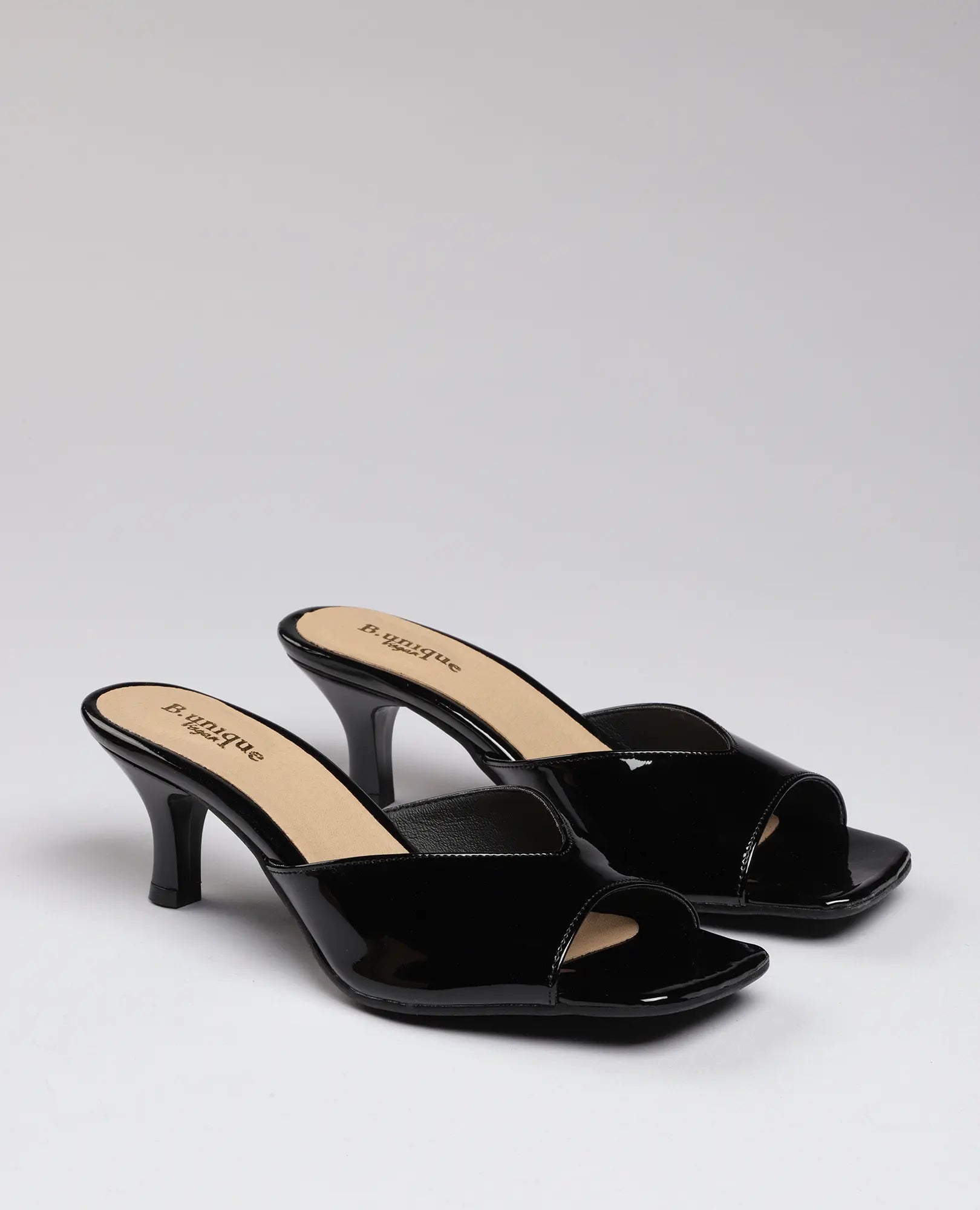 זוג כפכפי עקב-מנור של B-Unique VEGAN בצבע שחור מבריק דמוי עור לכה עם אצבעות פתוחות, על רקע בהיר אחיד.