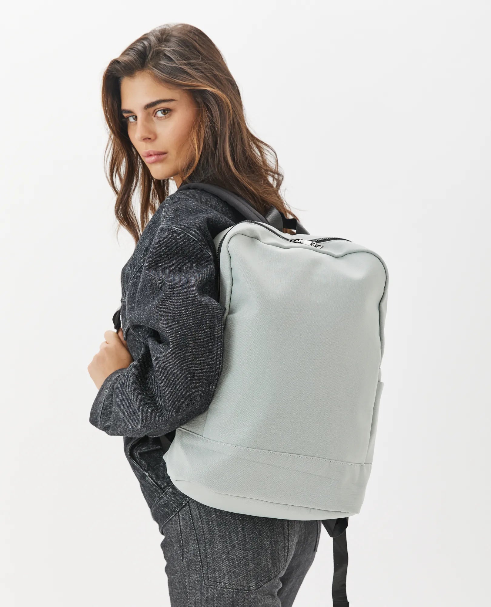 אישה עם שיער חום ארוך באפור בהיר תיק גב- נועה מבית B-Unique Bags, מביטה מעבר לכתפה.