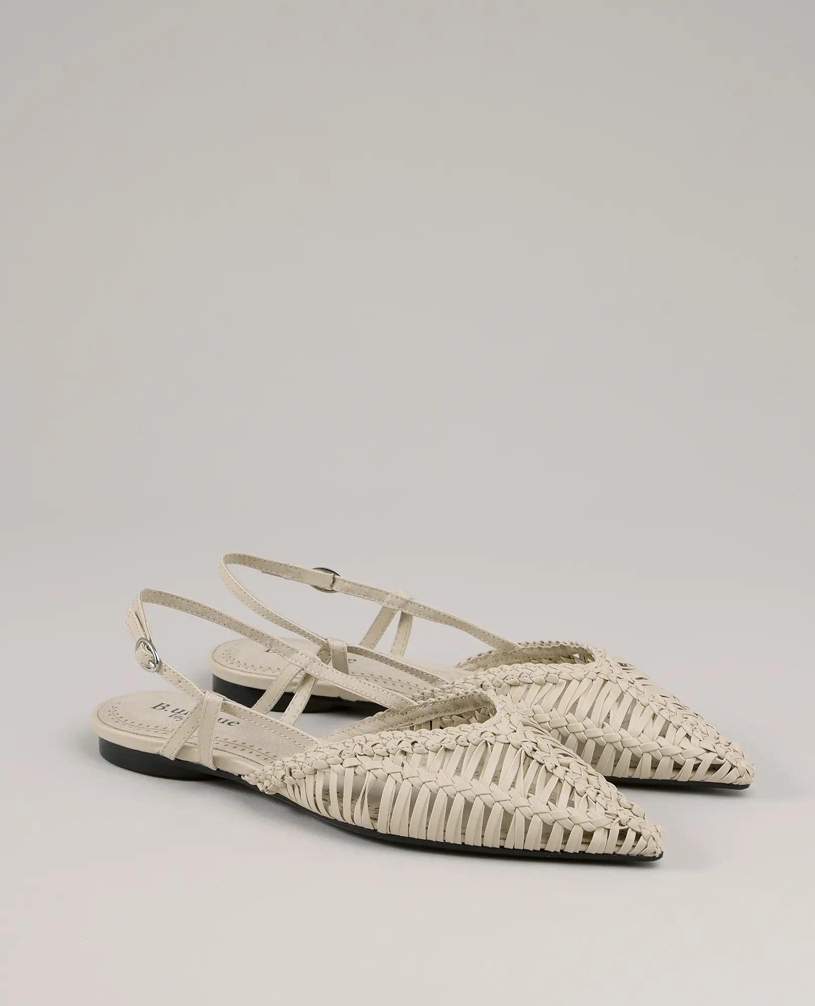 זוג נעליים שטוחות בצבע בז' של המותג B-Unique VEGAN, עם קצות מחודדים וסוליות שחורות נמוכות על רקע ניטרלי.