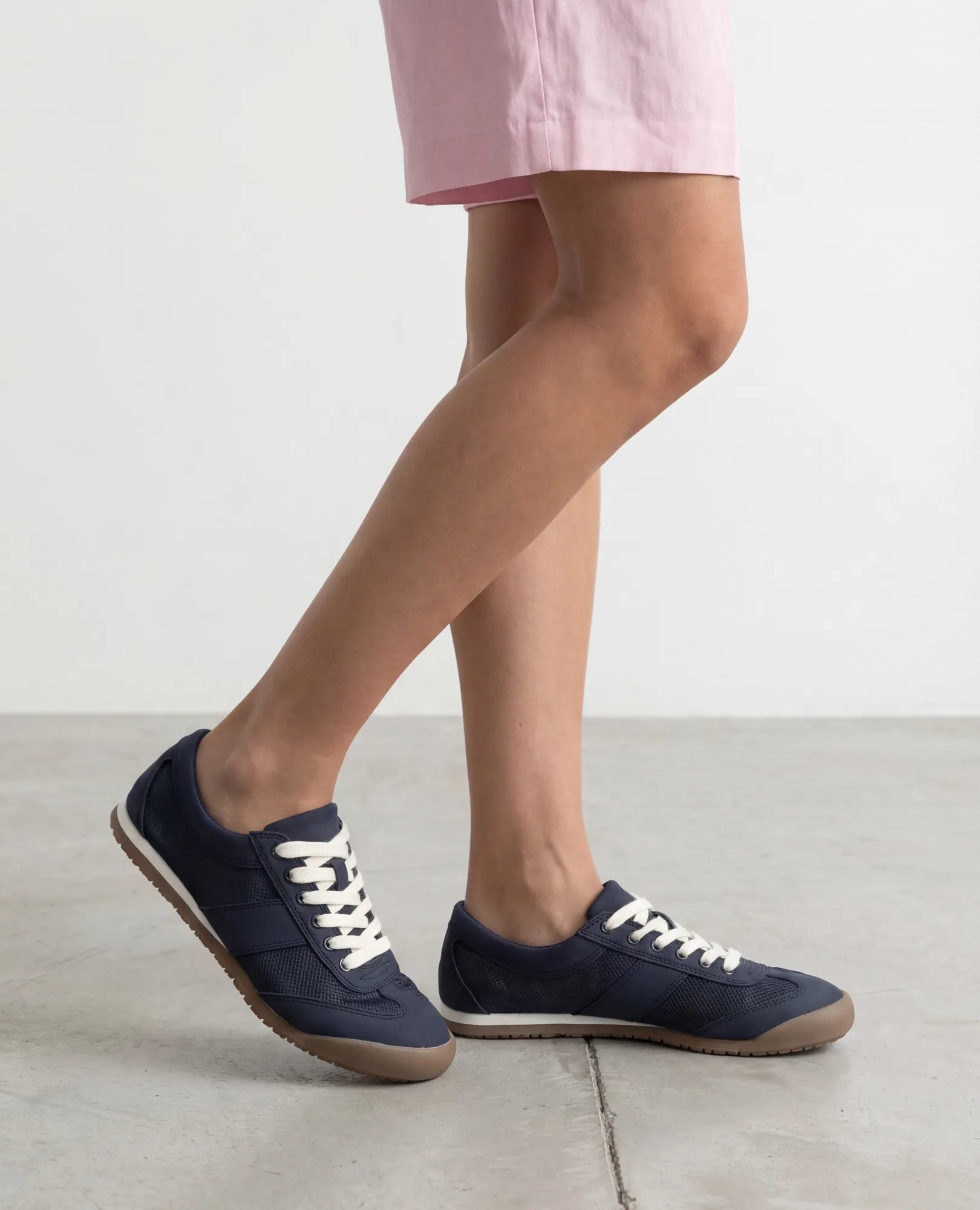 אישה לובשת שורטס ורוד בהיר ונעלי סניקרס- טניה מבית B-Unique VEGAN עומדת על רצפת בטון.