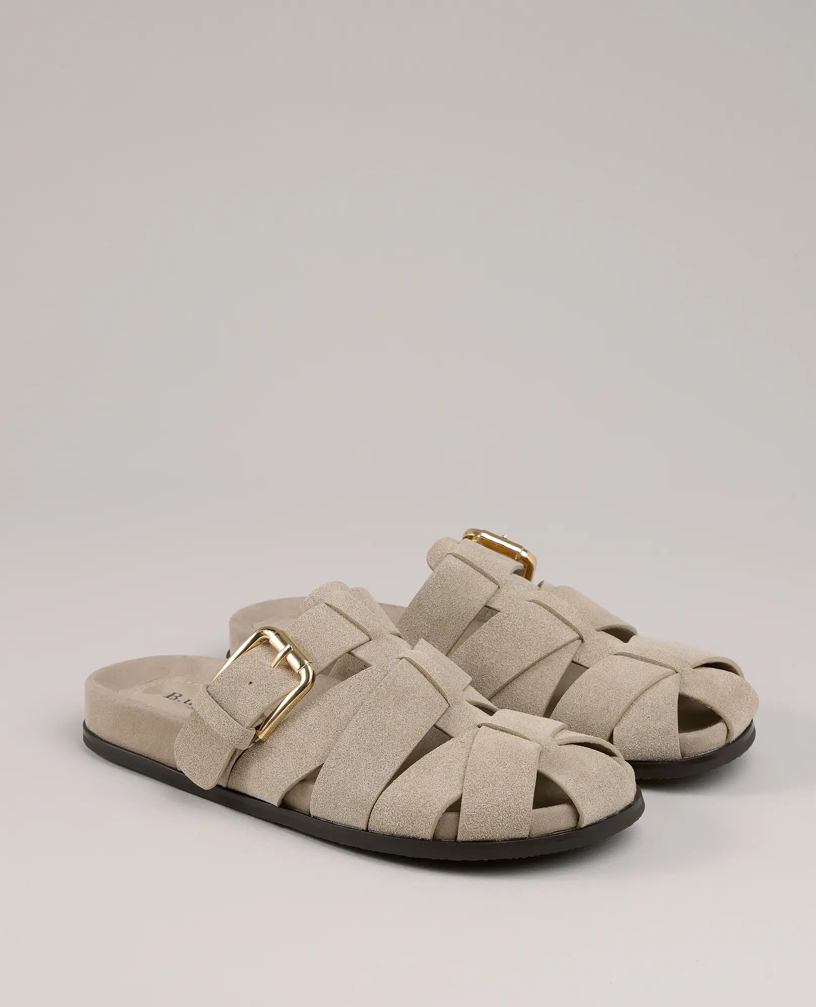 זוג כפכפי עור של B.unique - דגם "הוד" בצבע טאופ, עם רצועות מצטלבות ואבזמים מוזהבים, מוצגים על רקע אפור בהיר.