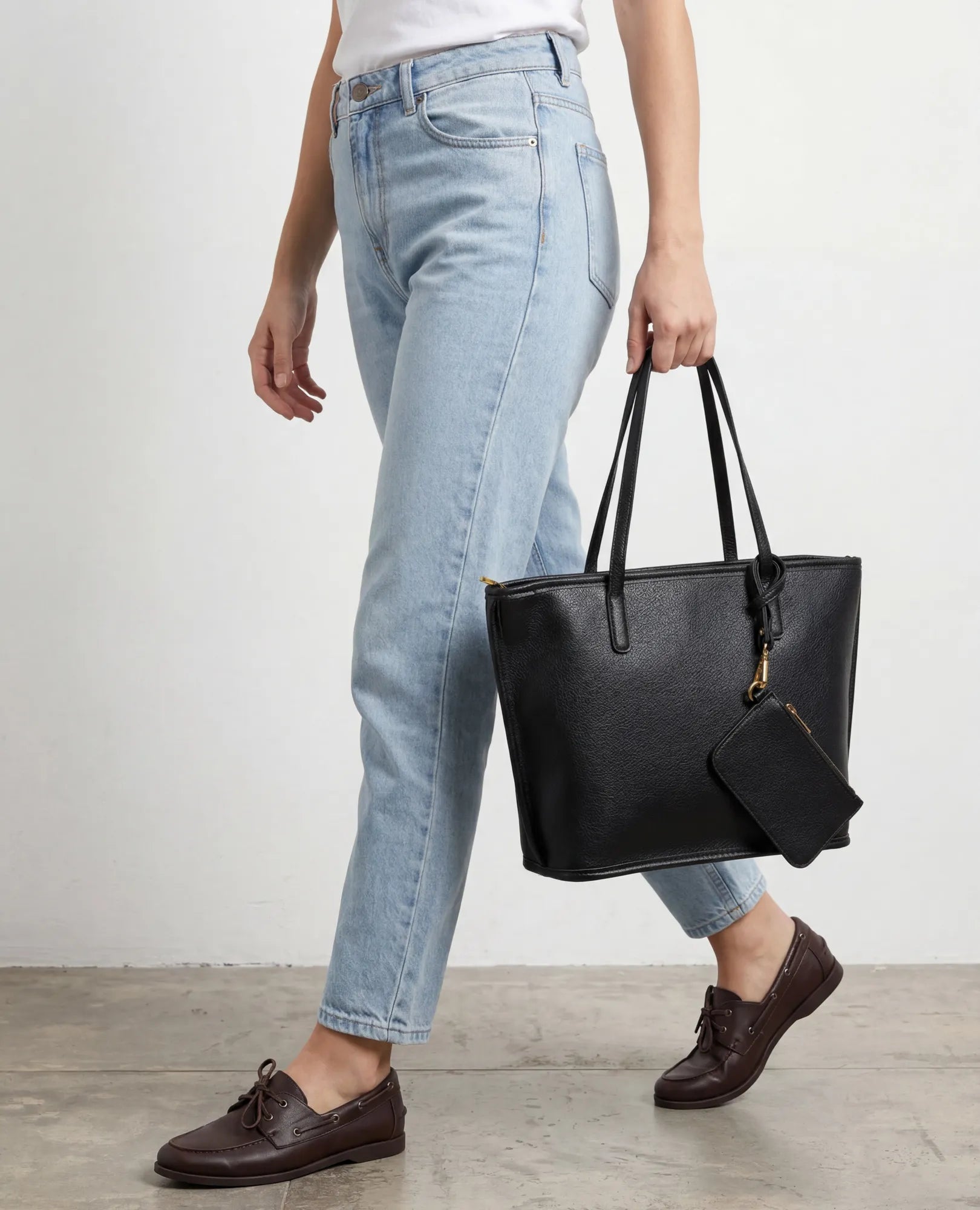 אישה עם תיק צד גדול ובו ארנק "רומא" מבית B-Unique Bags, נכנסת לבניין, לבושה בג'ינס.