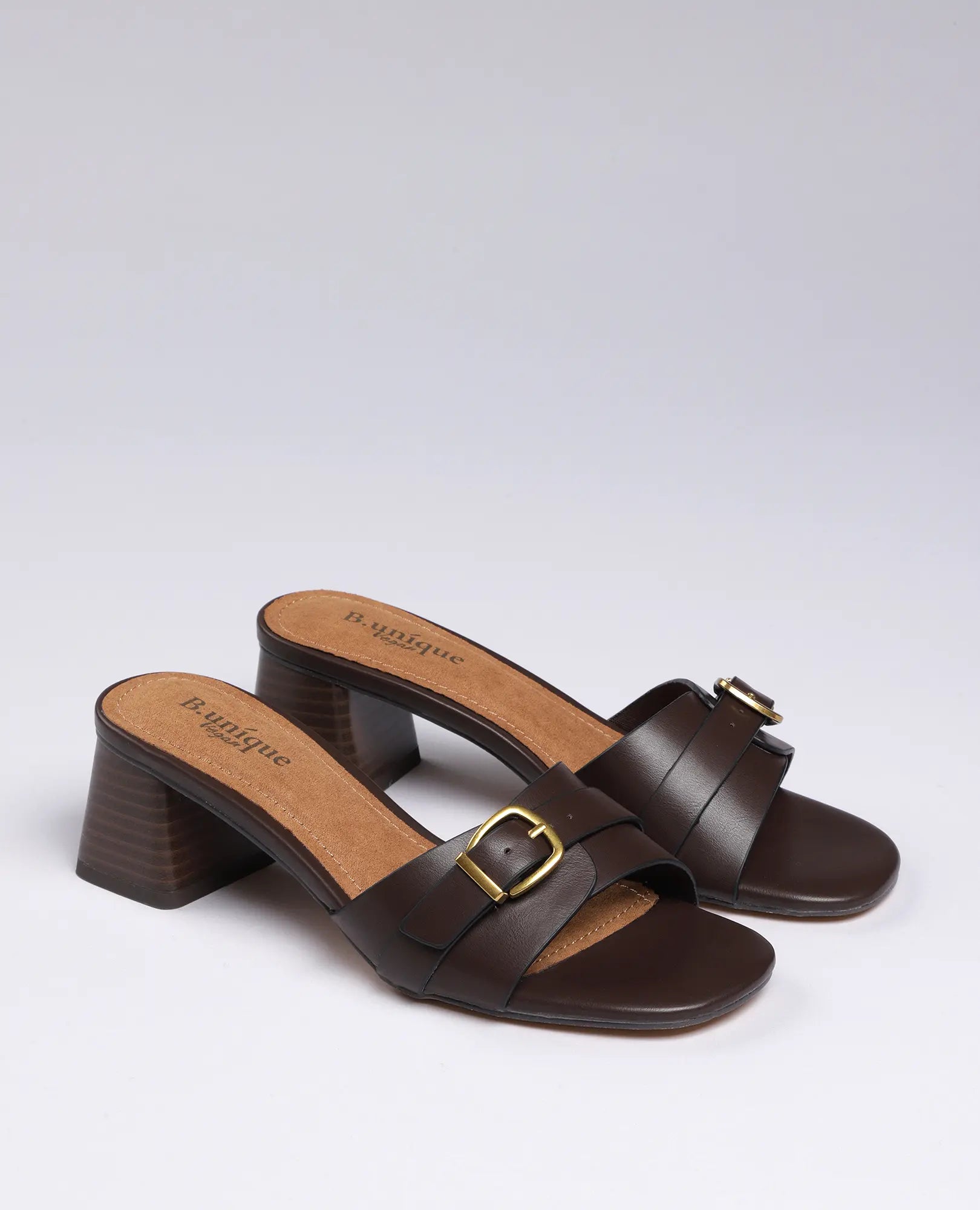 כפכפי עקב של B-Unique VEGAN בצבע קפה, עם רצועות רחבות ועיצוב שיקי, מוצגים על רקע חלק.