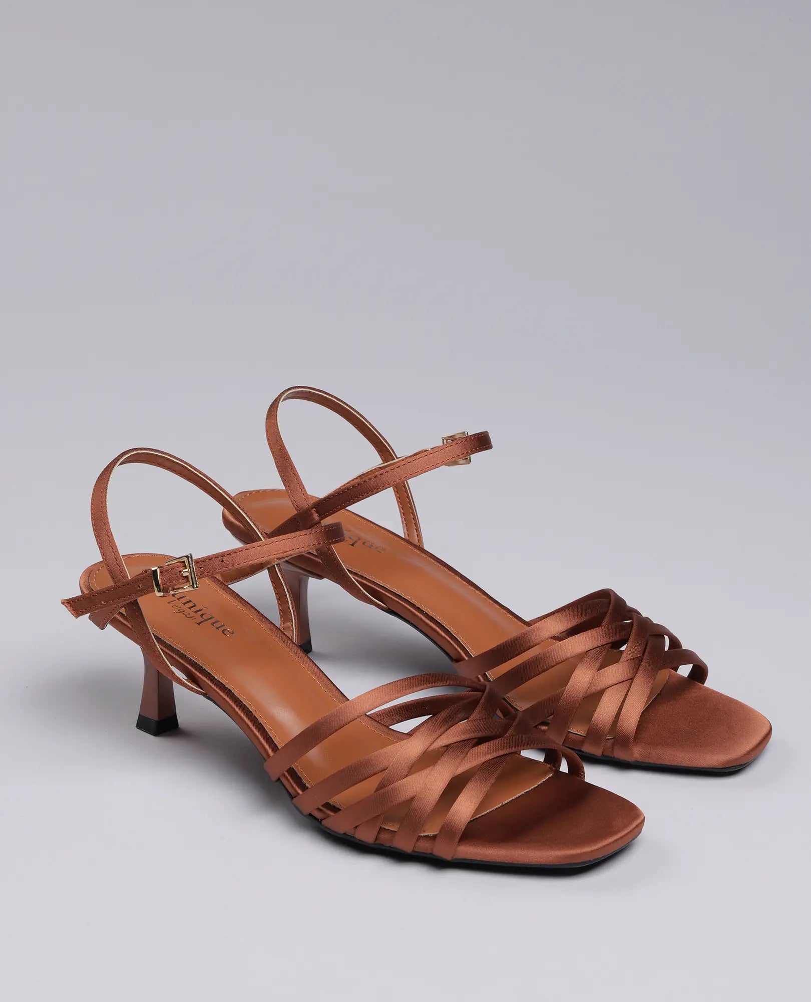 זוג סנדלי עקב "ברקת" מבית B-Unique VEGAN בצבע קאמל, עם רצועות בקרסול ואצבעות פתוחות, על רקע בהיר וחלק.