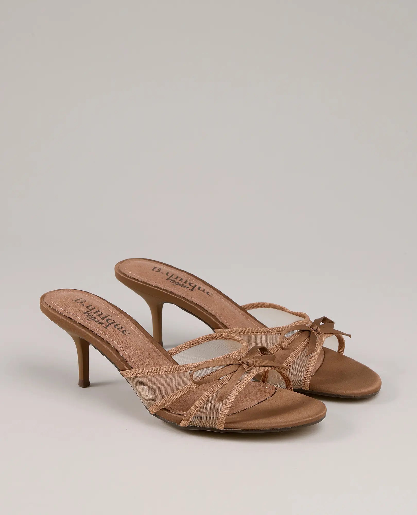 כפכפי עקב מפוארים של B-Unique VEGAN בצבע טאן עם רצועות דקות ופפיון, מוצגים על רקע בהיר.