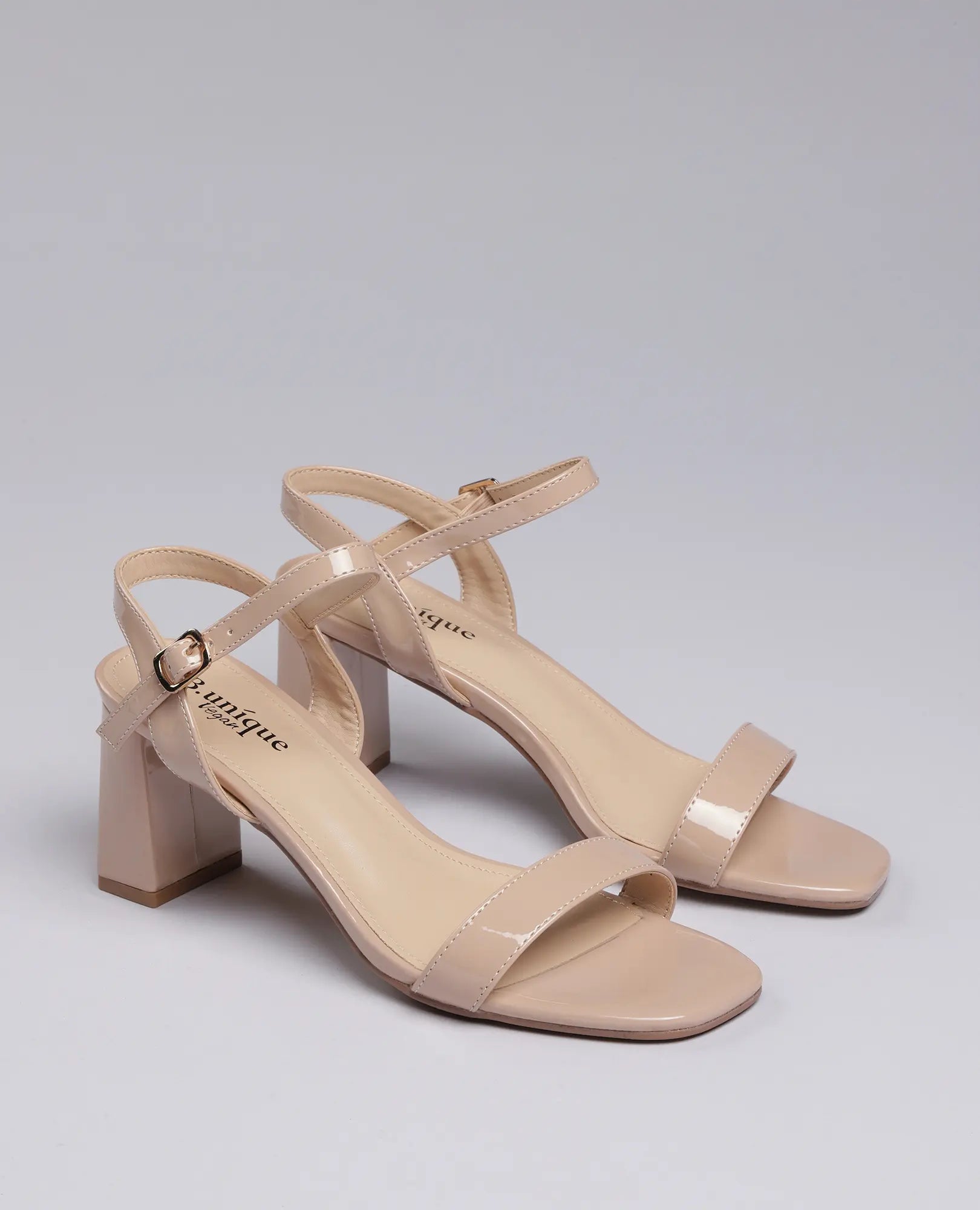 סנדלי עקב- אפריל של B-Unique VEGAN בצבע טאופ עם עקב רחב ורצועות קרסול, מוצגים על רקע אפור בהיר.