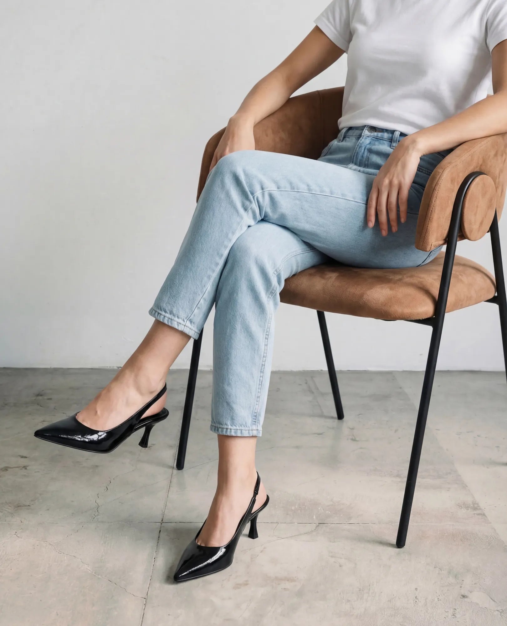 אדם בחולצה לבנה וג'ינס בהיר יושב על כיסא, נועל נעלי עקב שפיץ- דורון של B-Unique VEGAN.