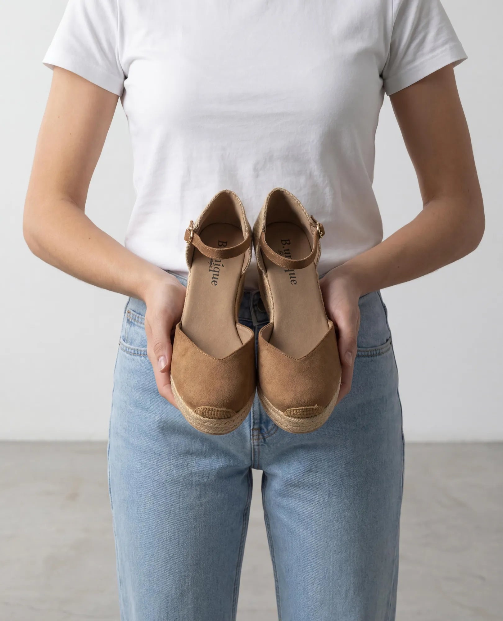 אדם לבוש בג'ינס וחולצה לבנה מחזיק את נעלי הפלטפורמה B-Unique VEGAN - כרם עם רצועת קרסול מול חזהו.