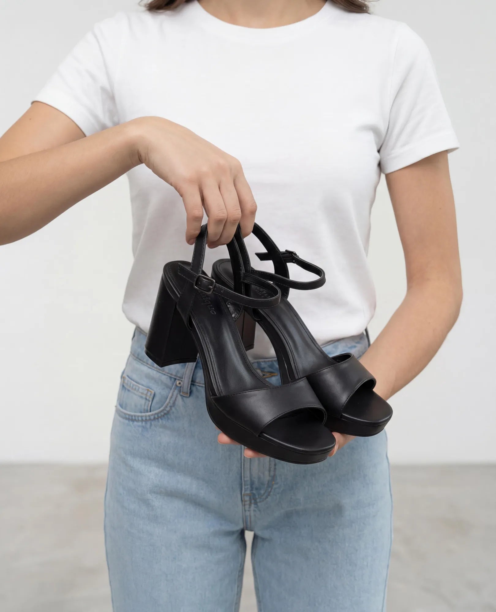 אדם לבוש בחולצת טי לבנה ובג'ינס נועל סנדלי פלטפורמה - "אניטה" מבית B-Unique VEGAN בצבע שחור, עם עקבים רחבים ורצועות בקרסול.